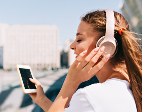 smiling-and-dancing-young-woman-holding-smartphone-and-listening-music-in-headphones